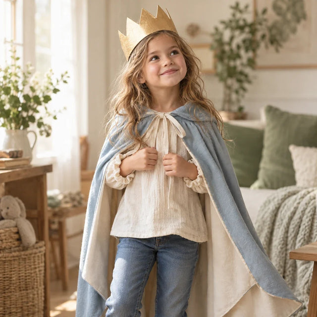 Et barn leker prinsesse med krone og kappe